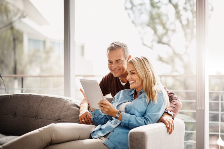 Fröhliches Paar sitzt auf einem Sofa und schaut auf ein Tablet